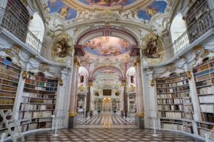 Biblioteca dell’abbazia di Admont con scaffali bianchi e dorati, affreschi sulle volte e luce dalle finestre