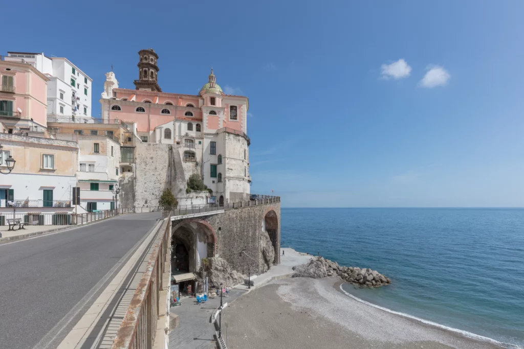 Veduta di Atrani con le case e una chiesa affacciate sulla strada costiera, gli archi e la spiaggia