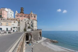 Veduta di Atrani con le case e una chiesa affacciate sulla strada costiera, gli archi e la spiaggia